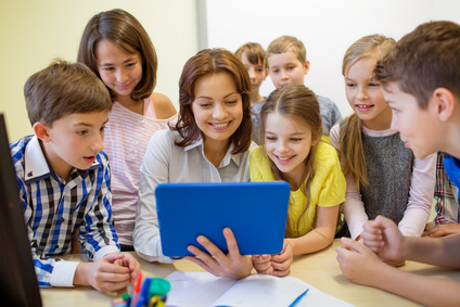 Photo d'une classe avec la maîtresse et les enfants apprenant en regardant une tablette