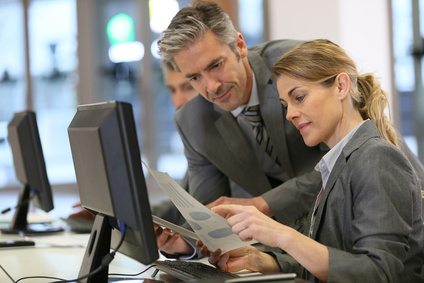 femme au travail assise face à un écran d'ordinateur homme à côté